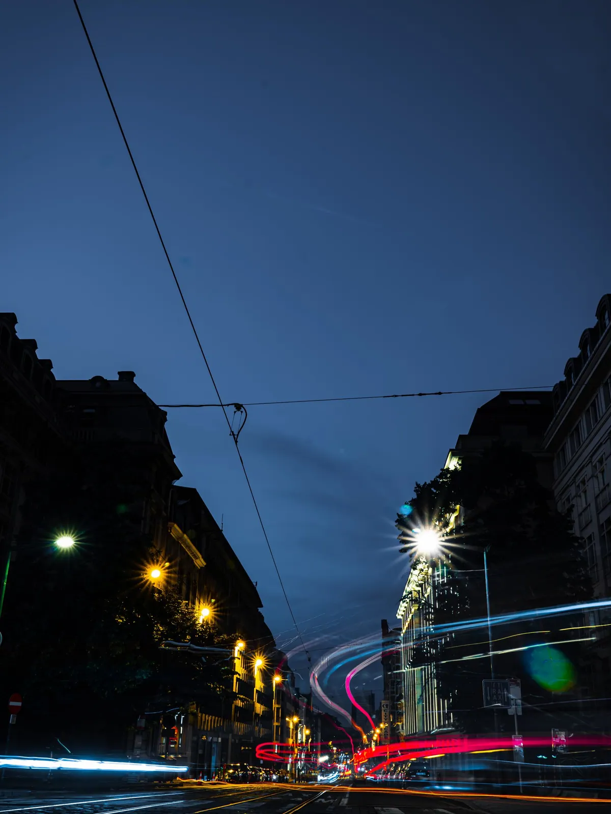 Rue bruxelloise en pose longue avec des traînées lumineuses bleues, rouges et jaunes
